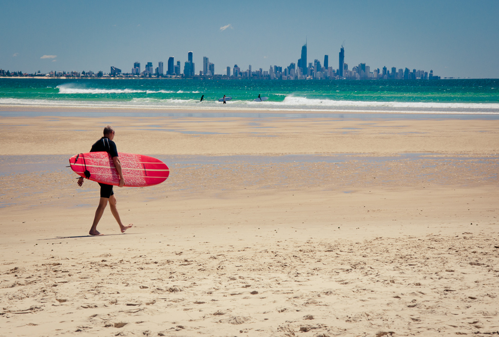 A surfer heading out at Currumbin beach with the Gold Coast skyline in the background