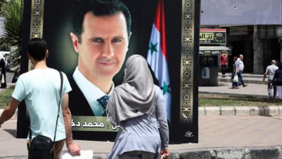 أشخاص يمشون أمام صورة رئيس النظام السوري بشار الأسد في دمشق